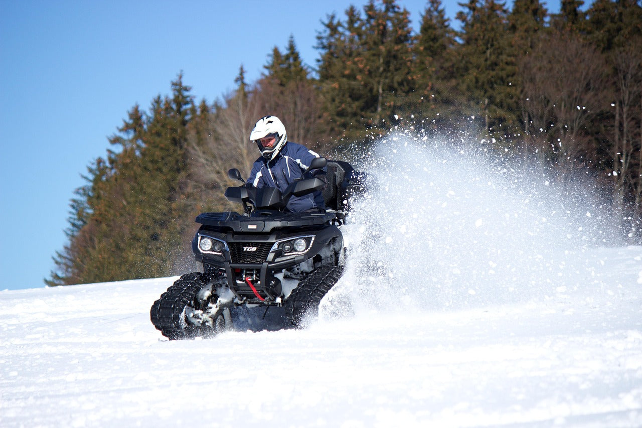ATV riding in winter snow with a rider using heated gear on a snow-covered trail